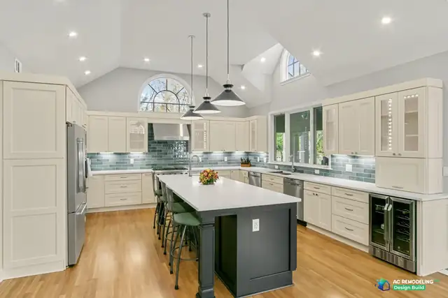 Vaulted white kitchen with cream shaker cabinets, a dark green island, black pendants and an arched window