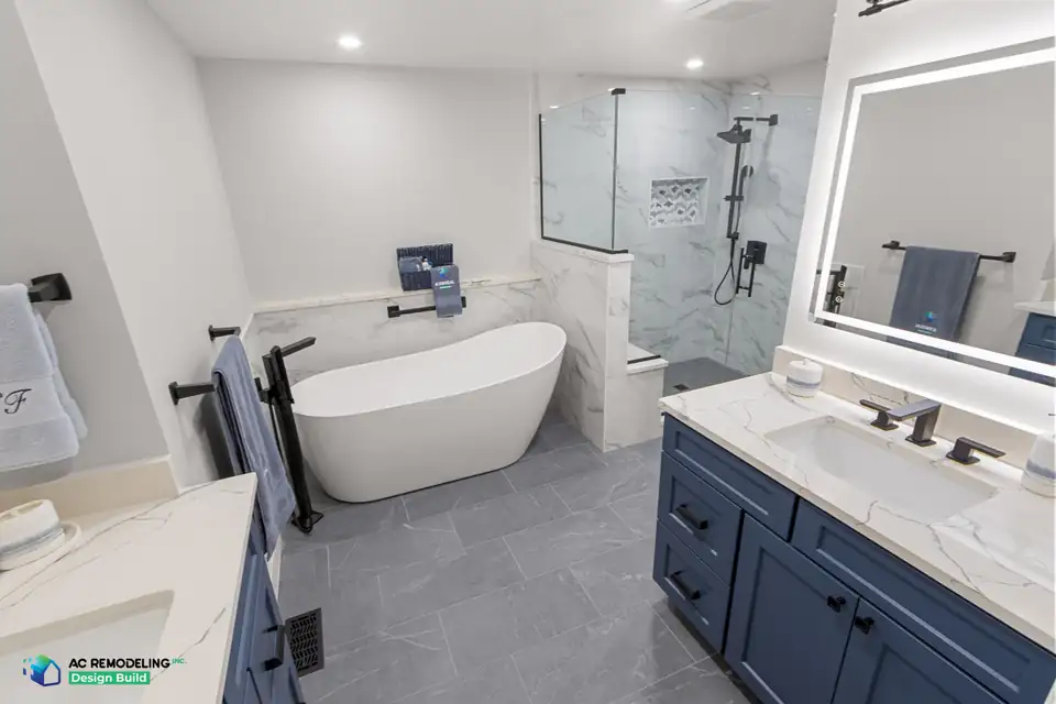 Design-build remodeling Gaithersburg MD: primary bath with freestanding soaking tub, marble-tiled walk-in shower and navy double vanities with backlit mirror