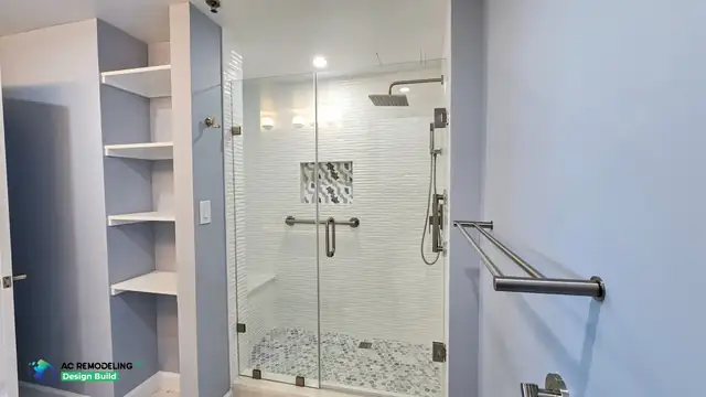 Frameless glass shower in Rockville, MD with wave-texture tile, mosaic niche, hex pebble floor and built-in shelving